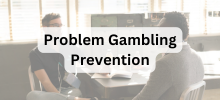Two people sitting at a table having a conversation in an office setting, with the text "Problem Gambling Prevention" displayed